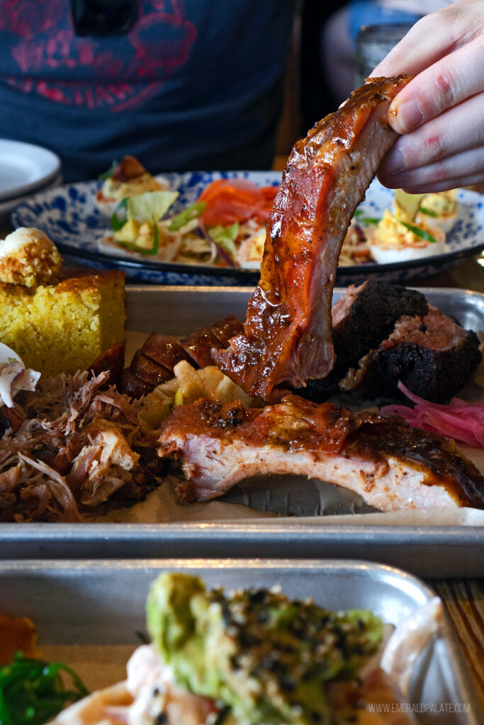person holding up a pork rib on a smoked meat platter