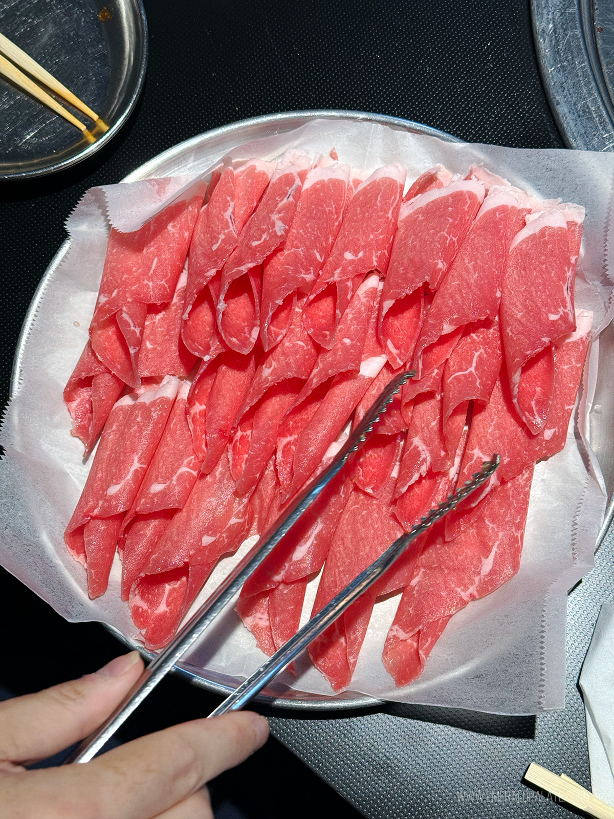 person using tongs to grab raw rolled beef