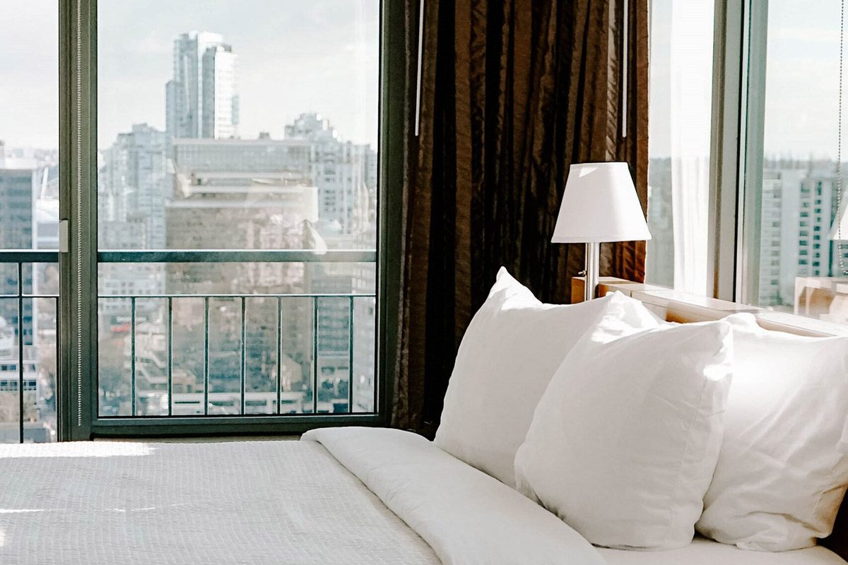 hotel room bed surrounded by windows overlooking downtown Vancouver BC 