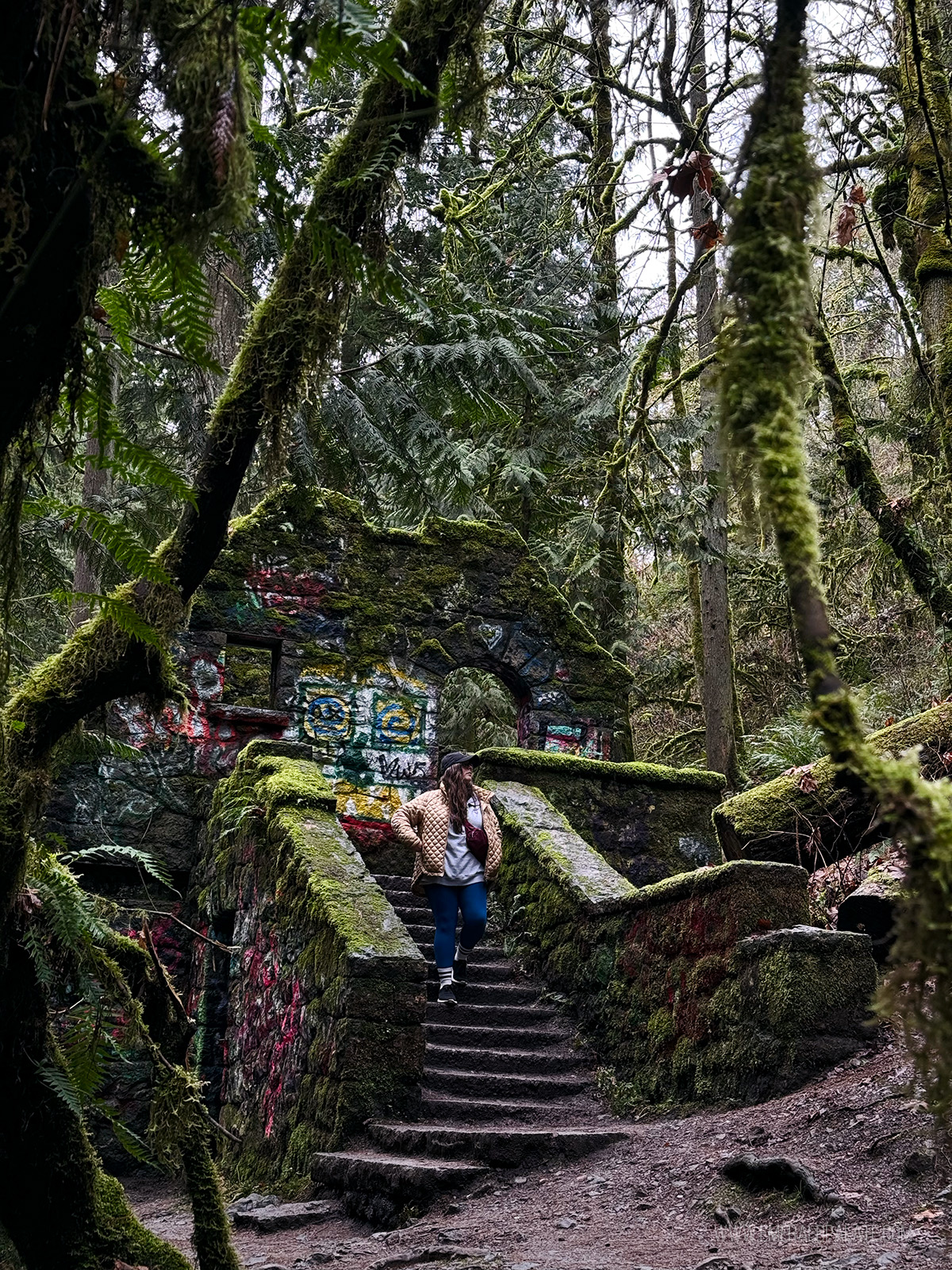 woman walking down the stairs of an abandoned stone building covered with graffiti in a PDX park