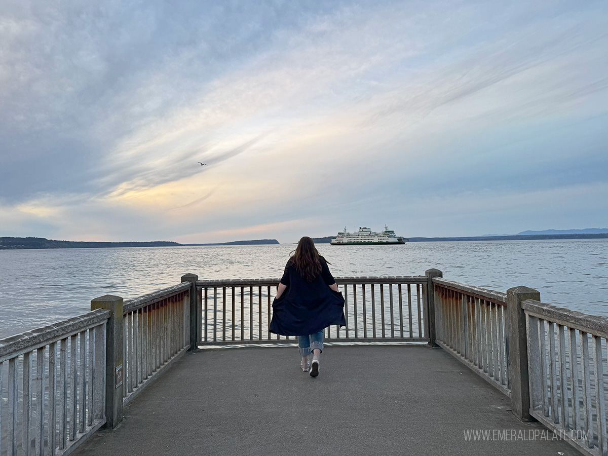 woman walking along a pier at sunset with Washington ferry in the distance