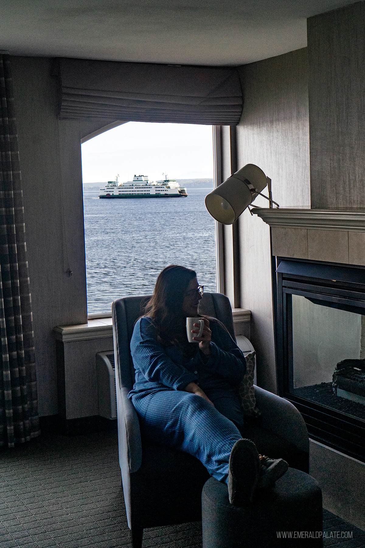 woman enjoying coffee in front of a hotel window with a WA ferry passing by