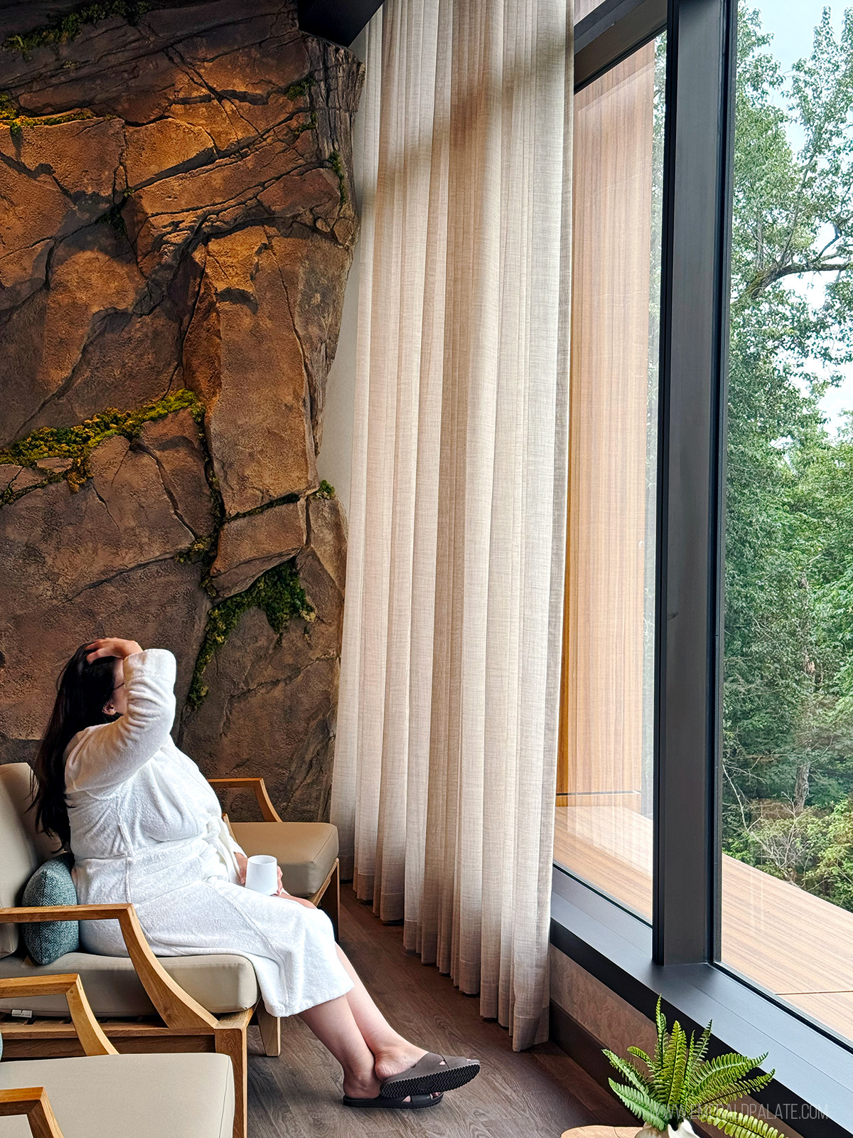 woman in robe looking out window into forest at one of the best spas in Seattle