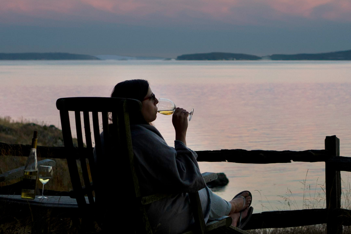 woman sipping wine at sunset overlooking the water, one of the best Pacific Northwest vacation ideas